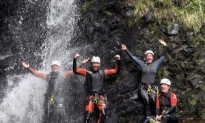 A group of canyoners cheering together under a waterfall at the end of a canyoning adventure.