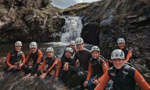 Gorge scrambling in Scotland - group resting in front of a scenic waterfall